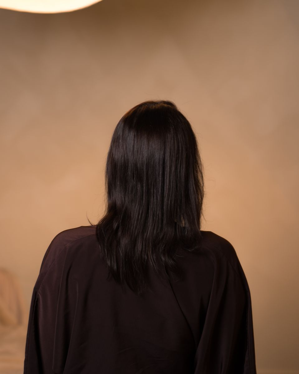 A Studio Beige client with shoulder-length dark hair from behind, before her extensions