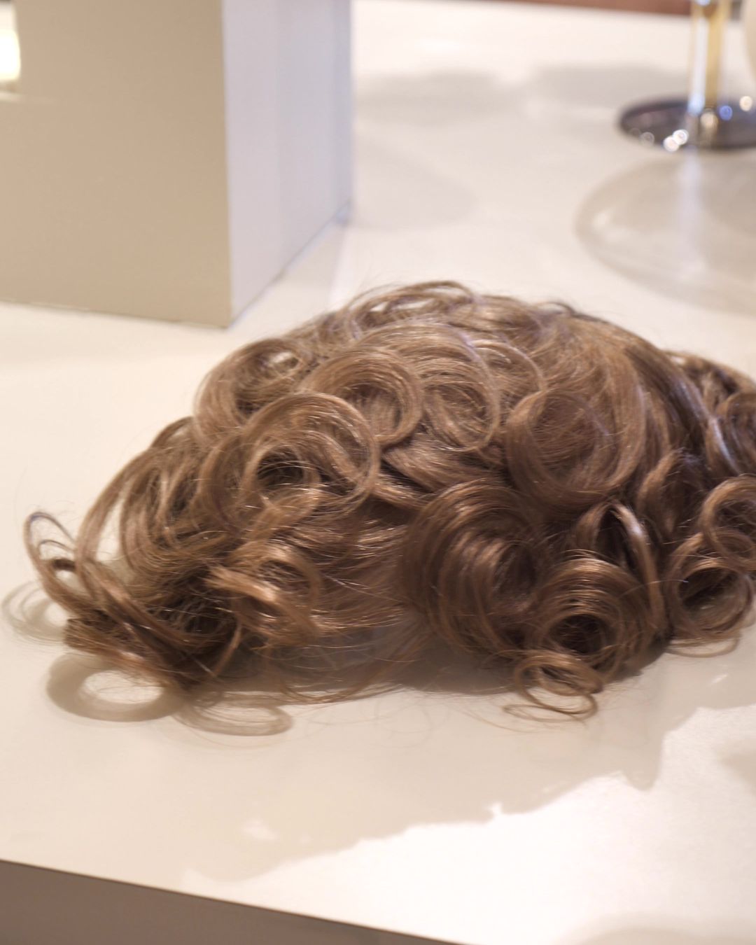 A men's hair system with natural curl resting on a styling counter at Studio Beige